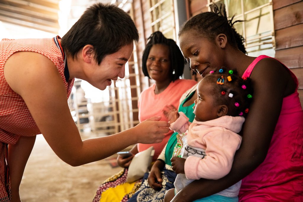 Dr. Munguu Khuyag-Ochir, a UNC Gillings student, greets a young patient in Zambia being held in a woman's arms.