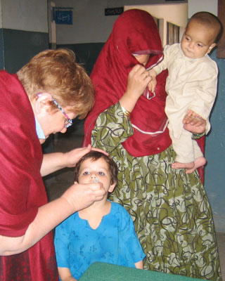 Cathy Jane Bowes, at left, administers polio vaccine to a young child in a Rawalpindi, Pakistan, train station in 2006. Photo by Qadeer Ahsan.