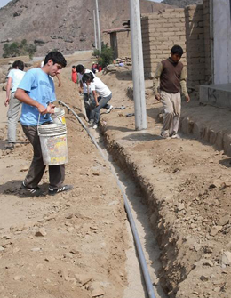 Students, with community members from Ciudad de Dios, Peru, line pipe trenches with sand to protect the pipes in the water distribution system.