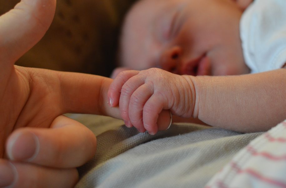 Adult holding sleeping baby's hand