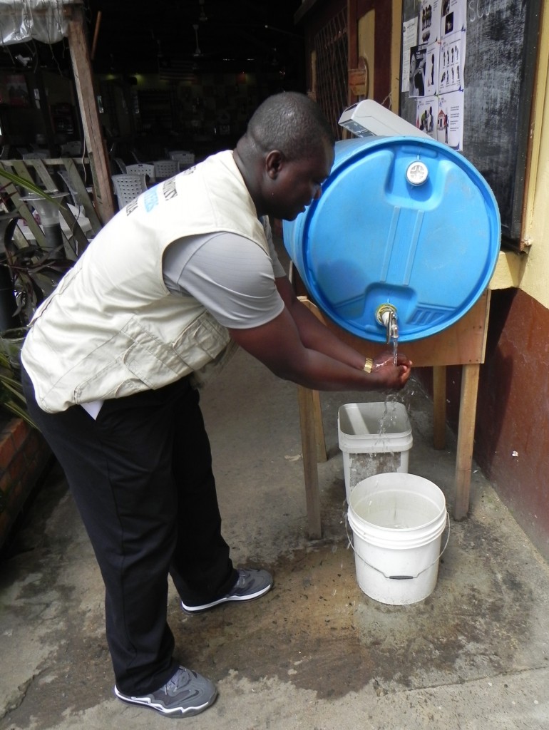 A clinic worker in Liberia sanitizes his hands at a chlorine hand-washing station. (Photo by William Brieger)