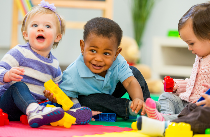 Three young children play with blocks in a child care facility.