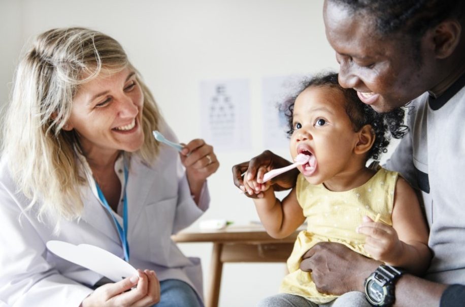 dentist teaching a child and her mother how to bruch the child's teeth