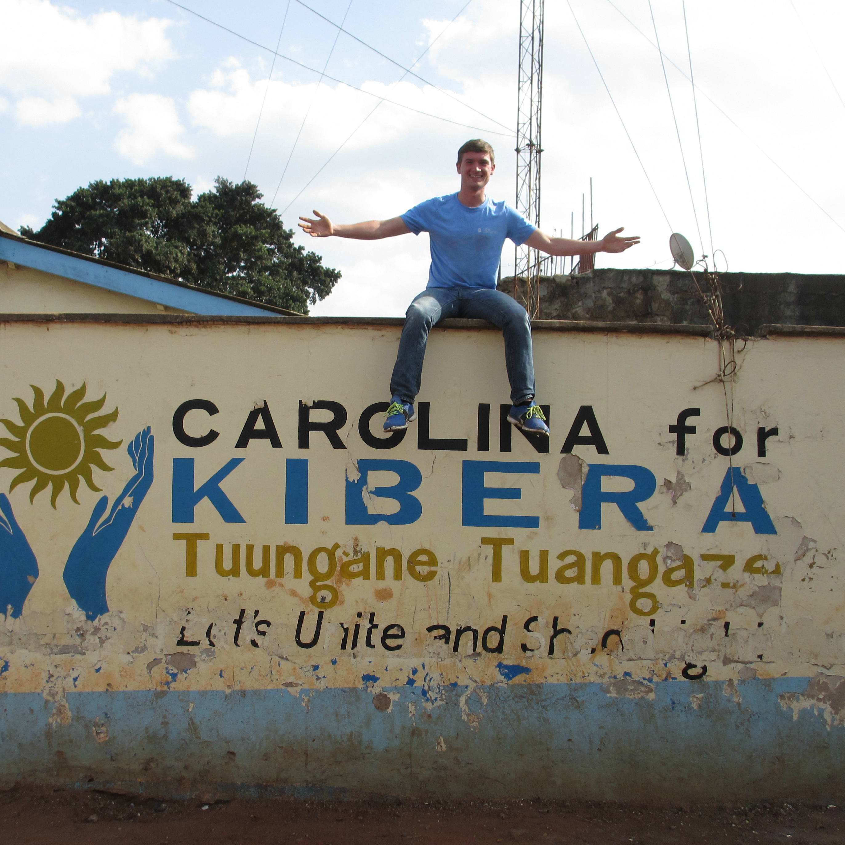 Jeffrey sits on a wall that reads "Carolina for Kibera."