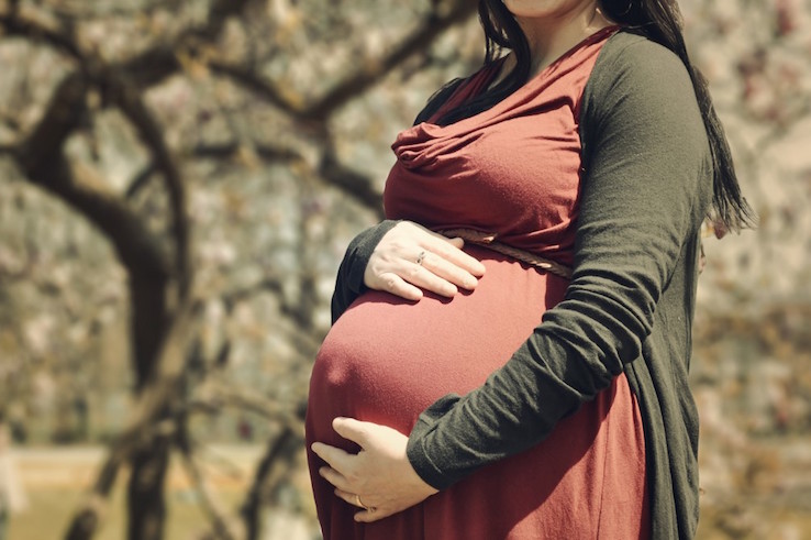 A pregnant woman stands outside while holding her belly.