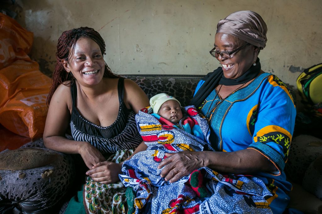 Two women smile with a newborn baby. (Photo credit: Harmony Chi)