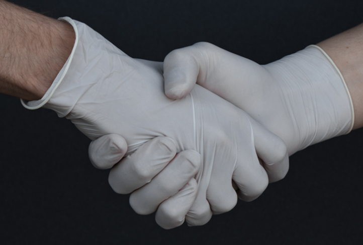 Two people wearing gloves clasp hands.