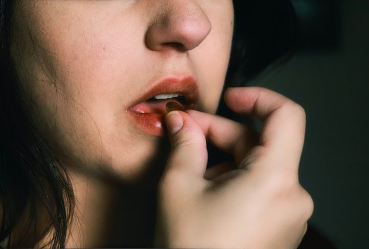 A woman puts a pill in her mouth.