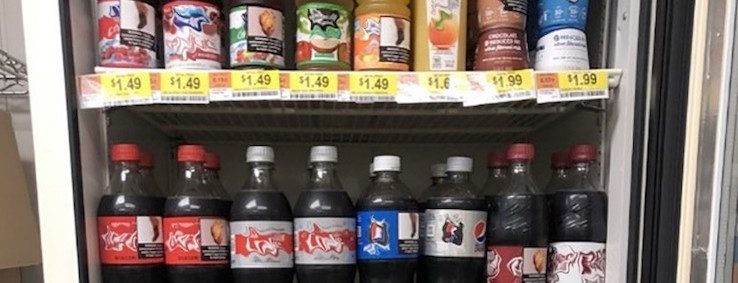 Sodas with warning labels fill a drink cooler.