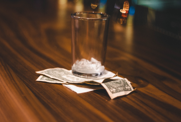 A glass with ice in it sits on top of a stack of dollar bills.