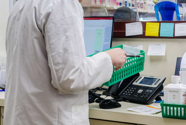 A pharmacist checks medication behind a pharmacy counter.