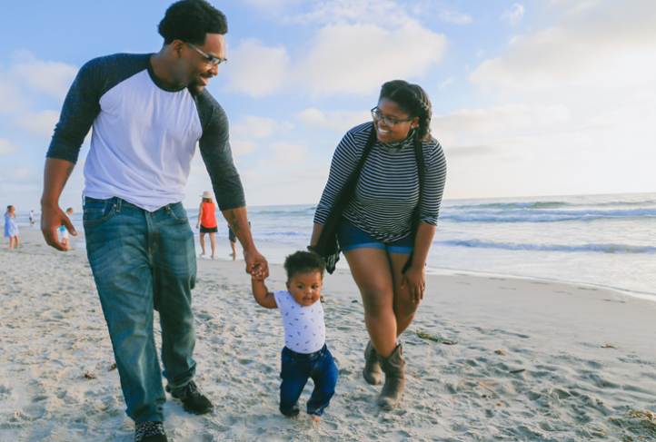 A family walks with their toddler on the beach.