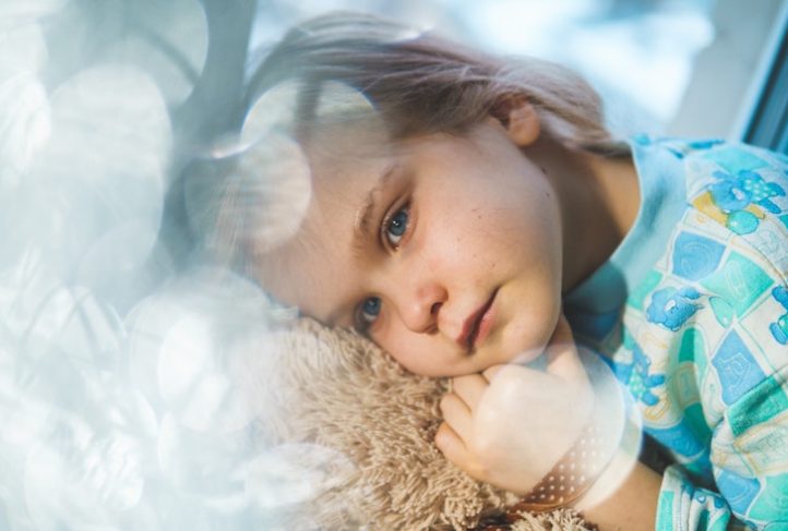 A sick child cuddles a stuffed animal.