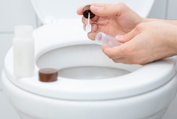 A person holding specimen over a toilet.