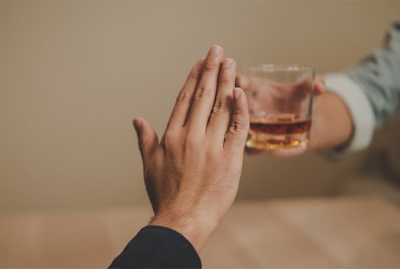 A person holding up their hand to a glass of alcohol.